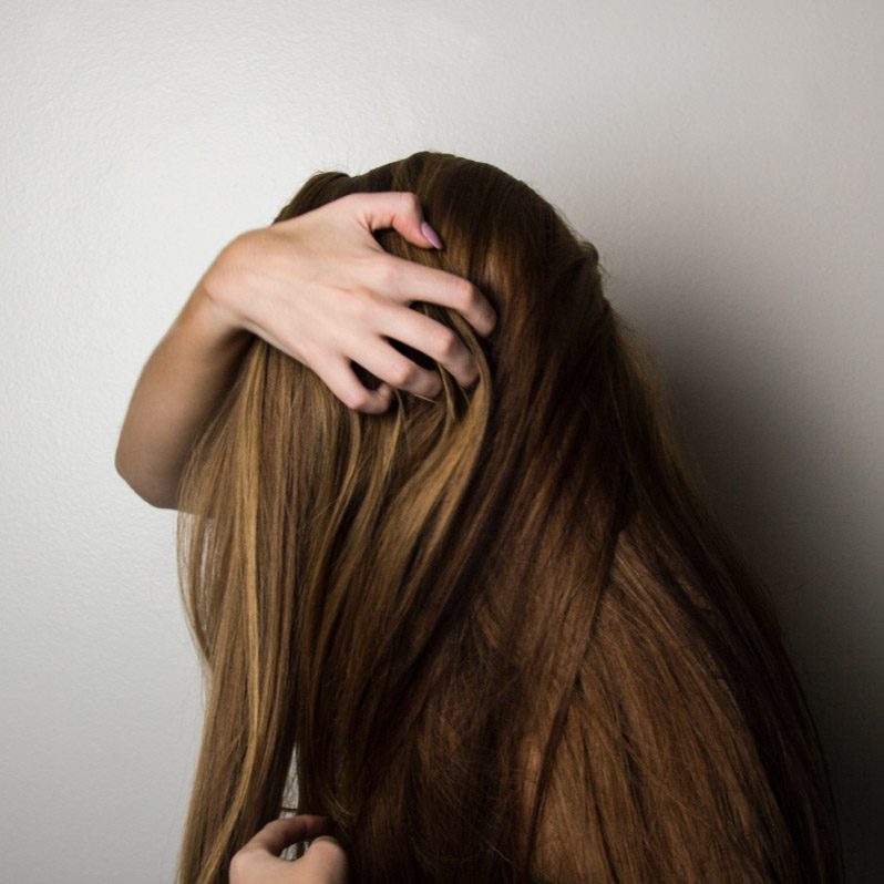 A woman with long brown hair is holding her head.