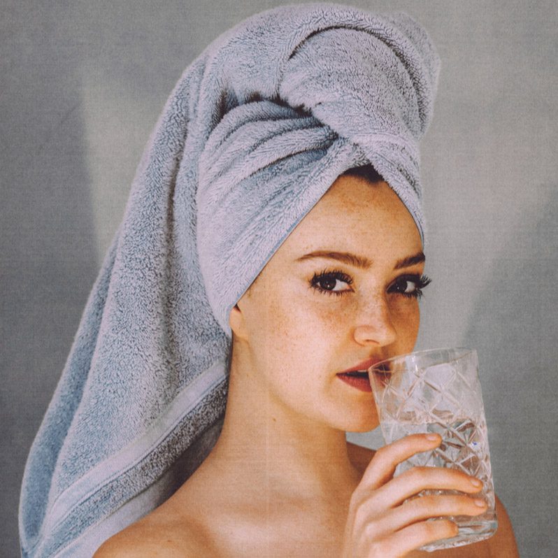 A woman with a towel on her head drinking water.